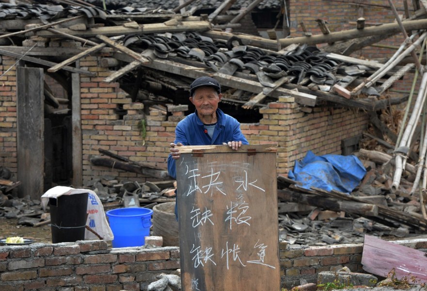 4月22日,雅安芦山县,一名老人在震毁的房屋前举牌写"缺水缺粮缺帐篷