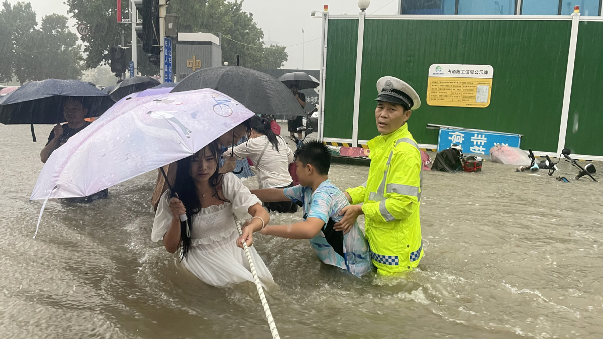Police help people cross flooded roads in C China's Zhengzhou
