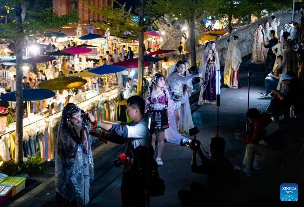 Tourists enjoy travel photo service at night fair in Jinghong City, SW China