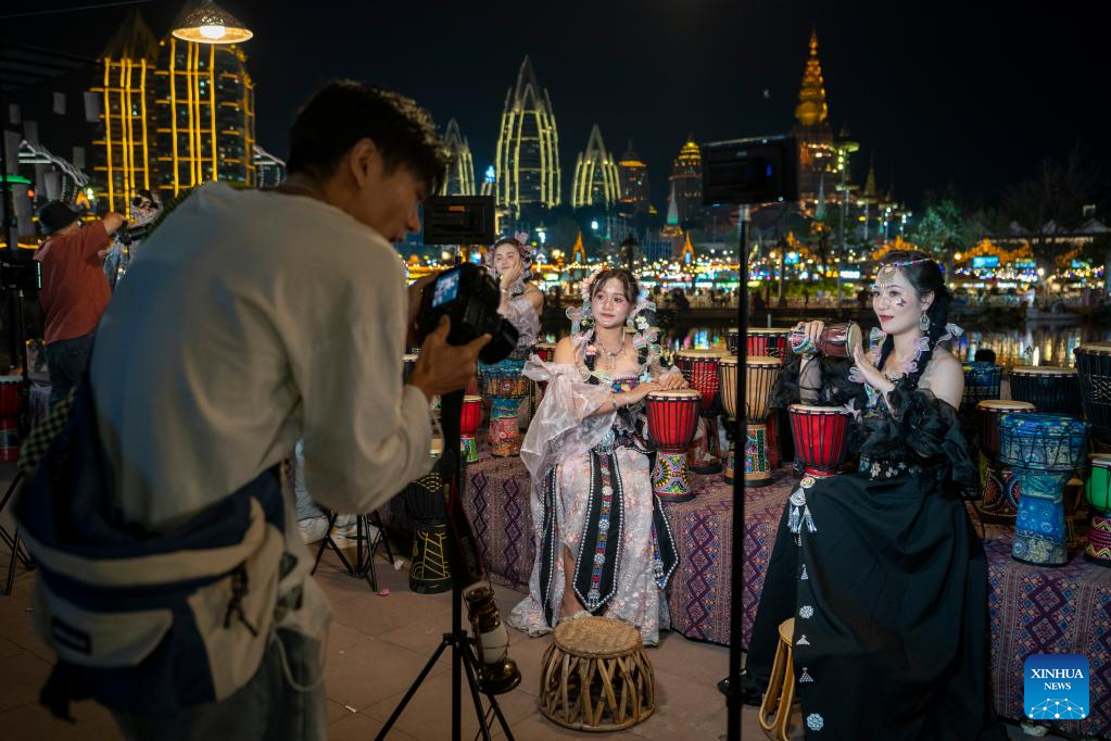 Tourists enjoy travel photo service at night fair in Jinghong City, SW China
